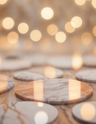 The primary subject of the image is a collection of round, marbled-looking objects, possibly coasters or decorative items, arranged on a wooden table. The setting is a room with a wooden floor, and the visual style appears to be a combination of a photo and digital art. The colors and mood of the image are warm and inviting, with the marbled objects and wooden table creating a sense of texture and depth.