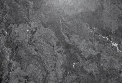 The image features a marble wall with a patterned texture. The primary subject is the marble wall, which is the main object, scene, or focus of the image. The setting/background is a marble wall, and the visual style is a photo. The colors and mood of the image are predominantly dark, with the marble wall being the main source of light and contrast.
