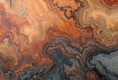 The primary subject of the image is a close-up of a marble stone with a unique and intricate pattern. The setting is a natural environment, possibly a rock formation or a stone surface. The visual style is a close-up of the marble, showcasing its texture and details. The colors and mood of the image are predominantly dark and earthy tones, giving it a natural and rugged appearance.