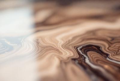 The primary subject of the image is a wooden table with a unique and intricate pattern on its surface. The table appears to be made of wood and has a natural texture. The setting is a room with a wooden floor, and the visual style is a close-up of the table, showcasing its distinctive design. The colors and mood of the image are warm and inviting, with the wooden table serving as the focal point of the scene.