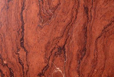 The primary subject of the image is a close-up of a marbled red stone wall. The setting is a natural environment, with the stone wall being the main focus. The visual style is a photo, capturing the intricate details of the stone wall. The colors and mood of the image are predominantly red, giving it a warm and earthy atmosphere.