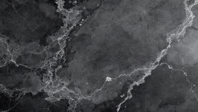 The primary subject of the image is a marble surface with a pattern of lines and curves. The setting is a black and white photograph, giving it a classic and timeless appearance. The visual style is a close-up of the marble surface, emphasizing the intricate details of the pattern. The colors and mood of the image are predominantly black and white, creating a sense of depth and contrast.
