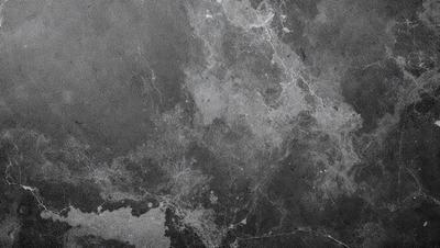 The primary subject of the image is a large, textured surface with a gray background. The setting appears to be a concrete or stone wall, possibly a part of a building. The visual style of the image is a combination of photo and digital art, creating a unique and intricate pattern. The dominant colors in the image are gray and black, giving it a moody and dramatic atmosphere.