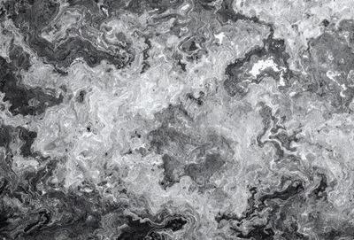 The primary subject of the image is a close-up of a rocky surface with a pattern of black and white. The setting is a rocky environment, and the visual style appears to be a combination of a photo and digital art. The dominant colors are black and white, creating a moody atmosphere.