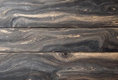 The primary subject of the image is a wooden surface with a unique and intricate pattern. The setting is a close-up view of the wooden surface, showcasing the details of the pattern. The visual style is a close-up of the wooden surface, which gives a sense of depth and texture. The colors and mood of the image are predominantly dark, with the wooden surface being the main focus.