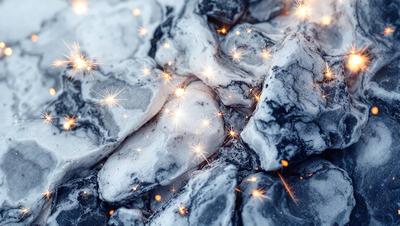 The primary subject of the image is a close-up of a rock with sparkling lights on it. The rock appears to be a marble or granite type, and the sparkling lights are likely the result of light reflecting off the rock's surface. The setting is outdoors, with the rock being the main focus of the image. The visual style is a close-up, which emphasizes the details of the rock and the sparkling lights. The colors in the image are predominantly dark, with the sparkling