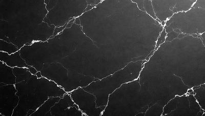 The primary subject of the image is a black marble countertop. The setting is a kitchen, with the countertop being the main focus of the scene. The visual style is a close-up of the marble countertop, showcasing its texture and details. The colors and mood of the image are predominantly dark, with the black marble countertop being the main source of contrast and visual interest.
