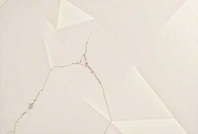 The primary subject of the image is a white wall with a brown spot, which appears to be a crack or a hole. The setting is a room with a white background. The visual style is a close-up of the wall, showcasing the brown spot. The colors and mood of the image are predominantly white and neutral, with the brown spot adding a touch of warmth and interest to the otherwise plain wall.