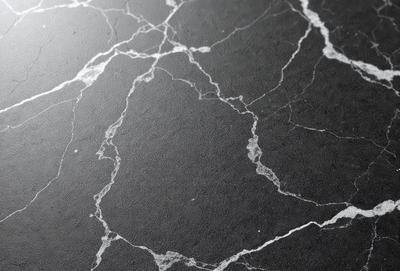 The primary subject of the image is a black marble countertop with a pattern of holes and ridges. The setting is a kitchen or bathroom counter, and the visual style is a close-up of the marble surface. The dominant colors are black and grey, giving the countertop a sleek and modern appearance.