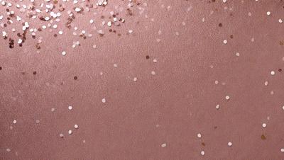The primary subject of the image is a close-up of a pink surface with a pattern of glittery gold confetti. The setting is a room with a pink background, and the visual style is a close-up of the pink surface with the confetti. The colors and mood of the image are predominantly pink and gold, creating a warm and festive atmosphere.