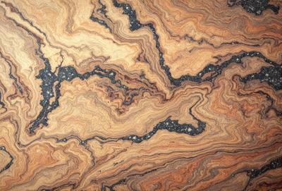 The primary subject of the image is a close-up of a marbled stone surface. The setting is a natural environment, possibly a rock formation or a stone wall. The visual style is a close-up of the stone, showcasing its unique texture and patterns. The colors and mood of the image are predominantly earthy tones, giving it a natural and organic feel.
