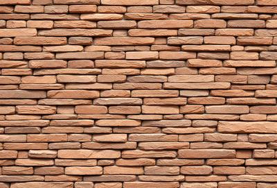 The primary subject of the image is a large brick wall, which is the main object, scene, or focus of the image. The setting/background features a rock wall, which is the environment, backdrop, or surface visible in the image. The visual style of the image is a photo, as it is a real-life brick wall. The colors and mood of the image are predominantly brown, giving it a natural and earthy appearance.