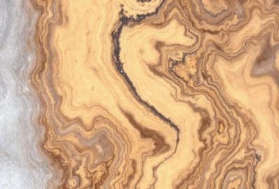 The primary subject of the image is a close-up of a marble surface with a unique and intricate pattern. The setting is a natural environment, possibly a rock formation or a stone wall. The visual style is a close-up of the marble, showcasing its texture and details. The colors and mood of the image are warm and earthy, with the marble's natural hues and patterns creating a sense of depth and complexity.
