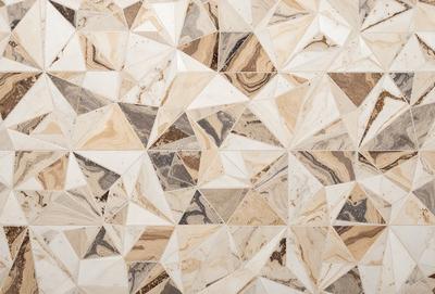 The primary subject of the image is a marble tile floor with a unique geometric pattern. The setting is a room with a marble wall, which complements the floor. The visual style is a close-up of the floor, showcasing the intricate design. The colors and mood of the image are predominantly neutral, with the marble tiles and wall providing a sense of elegance and sophistication.