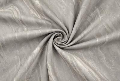 The primary subject of the image is a large piece of fabric, possibly a curtain or a sheet, with a pattern of swirls and spirals. The fabric is gray in color and appears to be made of silk. The setting is a room with a table, and the visual style is a close-up of the fabric. The colors and mood of the image are elegant and sophisticated, with the gray fabric and swirls creating a sense of luxury and refinement.