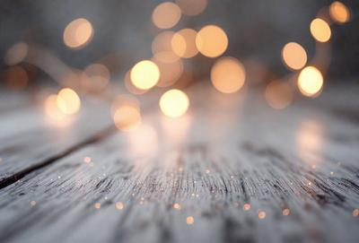 The primary subject of the image is a close-up of a wooden table with a pattern of lights on it. The setting is a room with a wooden floor, and the visual style appears to be a photo. The dominant colors in the image are the wooden table and the lights, creating a warm and inviting atmosphere.