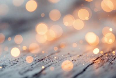 The primary subject of the image is a close-up of a wooden surface with a pattern of bright, colorful lights or sparkles. The setting is a wooden table, and the visual style appears to be a combination of a photo and digital art. The colors and mood of the image are vibrant and lively, with the bright lights creating a sense of energy and movement.