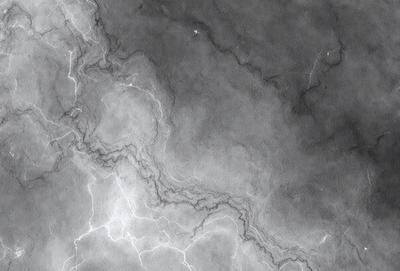 The primary subject of the image is a close-up of a marble surface with a pattern of light and dark streaks. The setting is a dark room, and the visual style appears to be a black and white photo. The colors and mood of the image are predominantly dark, with the light and dark streaks on the marble surface creating a contrasting pattern.