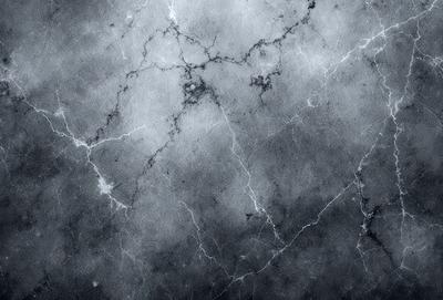 The primary subject of the image is a marble wall with a pattern of holes and lines. The setting is a dark room, and the visual style is a black and white photo. The dominant colors are black and white, and the overall atmosphere is moody and dramatic.