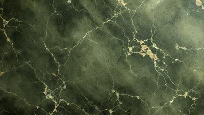 The image features a green marble wall with a pattern of yellow and brown spots. The wall appears to be textured and has a unique, natural appearance. The primary subject of the image is the marble wall, which serves as the main focus of the scene. The setting is indoors, likely in a room with a modern design. The visual style of the image is a close-up of the marble wall, showcasing its intricate patterns and textures. The colors and mood of the image are predomin