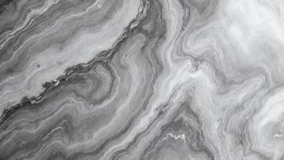 The primary subject of the image is a close-up of a marble surface with a patterned texture. The setting is a black and white photograph, which gives the image a classic and timeless appearance. The visual style is a combination of a photo and a drawing, creating a unique and artistic representation of the marble surface. The colors and mood of the image are predominantly black and white, with a touch of gray, giving it a sophisticated and elegant feel.