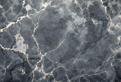 The primary subject of the image is a close-up of a marble wall with a pattern of swirls and bumps. The setting is a room with a gray marble wall, which serves as the background. The visual style is a close-up of the marble wall, showcasing its texture and pattern. The colors and mood of the image are predominantly gray, giving it a calm and sophisticated atmosphere.