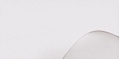 The primary subject of the image is a white paper with a curved edge. The setting is a white wall, and the visual style is a close-up of the paper. The colors and mood of the image are predominantly white, giving it a clean and minimalist appearance.