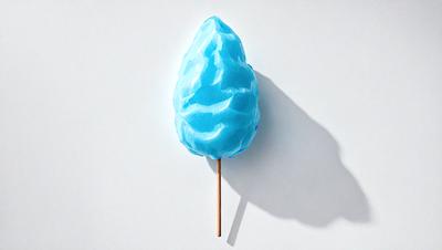 The primary subject of the image is a blue, plastic lollipop with a wooden stick. The lollipop is placed on a white surface, which serves as the setting or background. The visual style of the image is a photo, capturing the lollipop in its natural environment. The colors and mood of the image are predominantly blue and white, creating a clean and simple atmosphere.