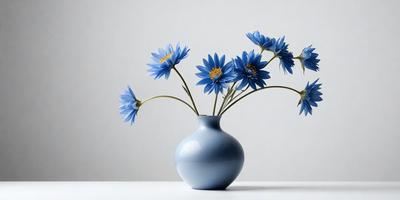 The primary subject of the image is a vase filled with blue flowers. The vase is placed on a white surface, which serves as the background. The visual style of the image is a photo, capturing the beauty of the flowers and the vase. The dominant colors in the image are blue and white, creating a calm and serene atmosphere.