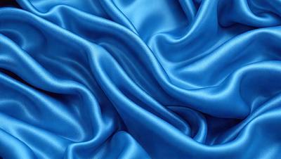 The primary subject of the image is a blue fabric, which appears to be a piece of silk. The setting is a close-up of the fabric, showcasing its texture and color. The visual style is a realistic representation of the fabric, with no indication of it being a photo, digital art, illustration, drawing, pattern, texture, or clipart. The dominant colors are blue and silver, creating a calm and serene atmosphere.