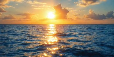 The primary subject of the image is the sunset over the ocean. The sun is setting behind the clouds, casting a warm glow over the water. The setting/background features the vast ocean with waves and clouds in the sky. The visual style of the image is a photo, capturing the beauty of the sunset and the serene atmosphere of the ocean. The colors and mood of the image are predominantly warm and calming, with the sunset creating a serene and peaceful scene.