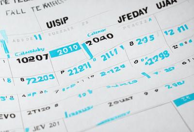 The primary subject of the image is a calendar, which is displayed on a white surface. The calendar is filled with blue numbers and letters, giving it a unique and colorful appearance. The setting appears to be a workspace or a personal space, as the calendar is placed on a table or a desk. The visual style of the image is a combination of digital art and illustration, as the calendar is drawn with a blue color palette. The overall atmosphere of the image is bright and cheerful, with the blue numbers and letters adding
