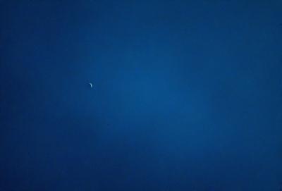 The primary subject of the image is the moon, which is visible in the sky. The setting is a dark blue sky, which creates a contrasting backdrop for the moon. The visual style of the image is a photo, capturing the moon in its natural environment. The colors and mood of the image are predominantly dark and moody, with the blue sky and the moon creating a sense of depth and tranquility.