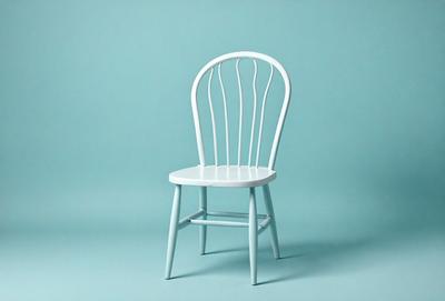 The primary subject of the image is a white chair with a blue background. The chair is a wooden, white, and blue chair with a wicker-like design. The setting is a blue background, which creates a contrast with the chair's colors. The visual style is a photo, capturing the chair's details and colors. The overall atmosphere is calm and inviting, with the blue background providing a soothing and relaxing environment.
