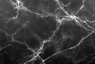 The primary subject of the image is a black and white marble wall with a pattern of white veins. The setting is a dark room, and the visual style is a close-up of the marble wall. The colors and mood of the image are predominantly dark and moody, with the white veins on the marble wall providing a contrasting element.