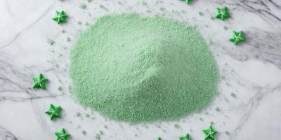 The primary subject of the image is a large pile of green powder, which appears to be a type of sugar or flour. The setting is a white surface, possibly a table or a counter, where the green powder is placed. The visual style of the image is a close-up of the green powder, showcasing its texture and color. The dominant colors in the image are green and white, creating a clean and fresh atmosphere.