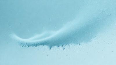 The primary subject of the image is a blue, foamy substance, possibly milk or a similar liquid, that is being poured or spilled onto a surface. The setting appears to be a white background, which contrasts with the blue substance. The visual style of the image is a close-up of the foamy substance, showcasing its texture and movement. The dominant colors in the image are blue and white, creating a calm and soothing atmosphere.