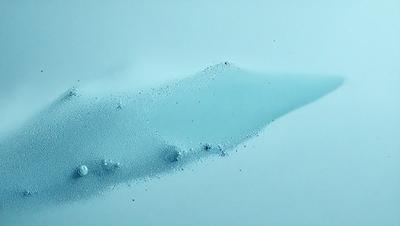 The primary subject of the image is a blue liquid, possibly water or a blue substance, that is dropping onto a white surface. The setting appears to be a white background, which contrasts with the blue liquid. The visual style of the image is a close-up of the dropping liquid, showcasing its movement and the white surface beneath it. The colors and mood of the image are predominantly blue and white, creating a sense of calm and tranquility.