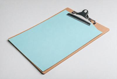 The primary subject of the image is a clipboard with a blue sheet of paper attached to it. The clipboard is placed on a white surface, which serves as the setting or background. The visual style of the image is a photo, capturing the details of the clipboard and the blue paper. The colors and mood of the image are predominantly white and blue, creating a clean and organized appearance.