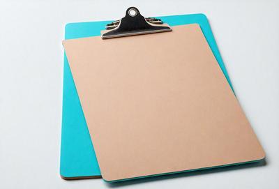 The primary subject of the image is a clipboard with a blue cover. The clipboard is attached to a metal clip, which is in turn attached to a piece of paper. The setting is a white background, and the visual style is a photo. The dominant colors are blue and white, creating a clean and professional atmosphere.