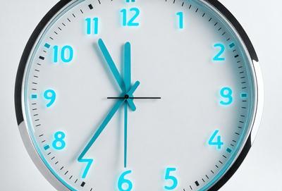 The primary subject of the image is a clock with a blue face and blue hands. The clock is set against a white background, giving it a clean and modern appearance. The visual style of the image is a close-up of the clock, emphasizing its details and design. The colors and mood of the image are predominantly blue, creating a calm and soothing atmosphere.