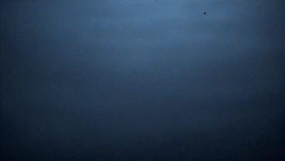 The primary subject of the image is a dark blue sky with a few clouds. The setting is a vast, open space with no visible landmarks or objects. The visual style is a natural, outdoor scene. The colors and mood are predominantly dark and moody, with the blue sky and clouds creating a sense of depth and vastness.