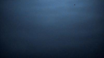 The primary subject of the image is a dark blue sky with a few clouds. The setting is a vast, open space with no visible landmarks or objects. The visual style is a natural, outdoor scene. The colors and mood are predominantly dark and moody, with the blue sky and clouds creating a sense of depth and vastness.