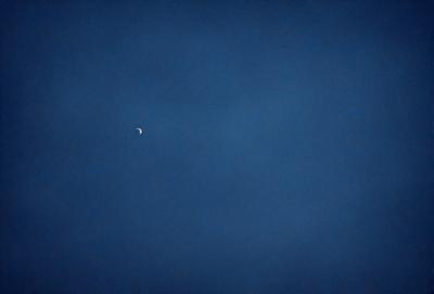 The primary subject of the image is a moon, which is visible in the sky. The setting is a dark blue sky, and the visual style appears to be a photo. The colors and mood of the image are predominantly dark and moody, with the moon being the main source of light in the scene.