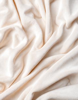 The primary subject of the image is a white sheet with a wrinkled texture. The sheet is draped over a bed, creating a cozy and comfortable atmosphere. The setting is a bedroom, with the bed being the main focus of the scene. The visual style is a close-up of the sheet, showcasing its wrinkled texture and the overall mood is warm and inviting.