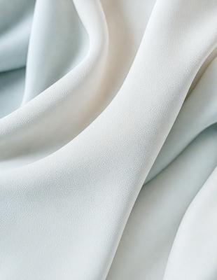 The primary subject of the image is a white sheet of fabric. The setting is a white background, which creates a clean and minimalist appearance. The visual style is a close-up of the fabric, showcasing its texture and details. The colors and mood of the image are predominantly white, giving it a calm and serene atmosphere.