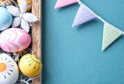 The primary subject of the image is a wooden shelf with a variety of colorful eggs and bunnies on it. The setting is a blue table, and the visual style appears to be a photo. The colors and mood of the image are vibrant and cheerful, with the eggs and bunnies adding a playful and festive touch to the scene.