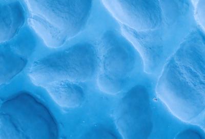 The primary subject of the image is a blue, textured surface with a pattern of white dots. The setting appears to be a blue ocean or a large body of water. The visual style of the image is a combination of a photo and a digital art or illustration, creating a unique and intriguing appearance. The dominant colors in the image are blue and white, with the blue surface and white dots creating a calming and serene atmosphere.