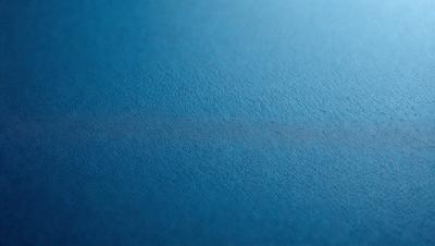 The primary subject of the image is a blue surface, which appears to be a piece of leather or a similar material. The setting is a close-up of the blue surface, with no background or additional elements visible. The visual style is a close-up, which emphasizes the texture and color of the blue material. The colors and mood of the image are predominantly blue, creating a calm and serene atmosphere.
