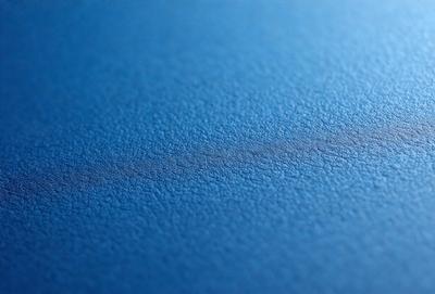 The primary subject of the image is a blue surface, possibly a table or a wall, with a dark blue streak or shadow running across it. The setting appears to be indoors, and the visual style is a close-up of the blue surface. The colors and mood of the image are predominantly dark and moody, with the blue surface contrasting with the dark blue streak.